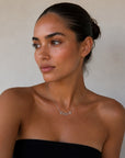 A woman wearing a black strapless tube top and white pants, wearing a delicate silver necklace with the name 'Cindy' on a light beige background.