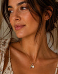 Woman wearing a necklace with a pendant, set against a neutral background
