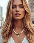 Woman with long blonde hair wearing a white top and necklace in an urban setting