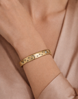 Gold bracelet with star and moon designs on a wrist against a soft pink background