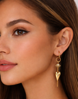 Close-up of a woman wearing gold earrings and a necklace with a plain background