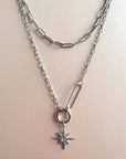 A double layer starburst pendant necklace with a silver outer chain and a shorter silver inner chain, featuring a starburst charm pendant.