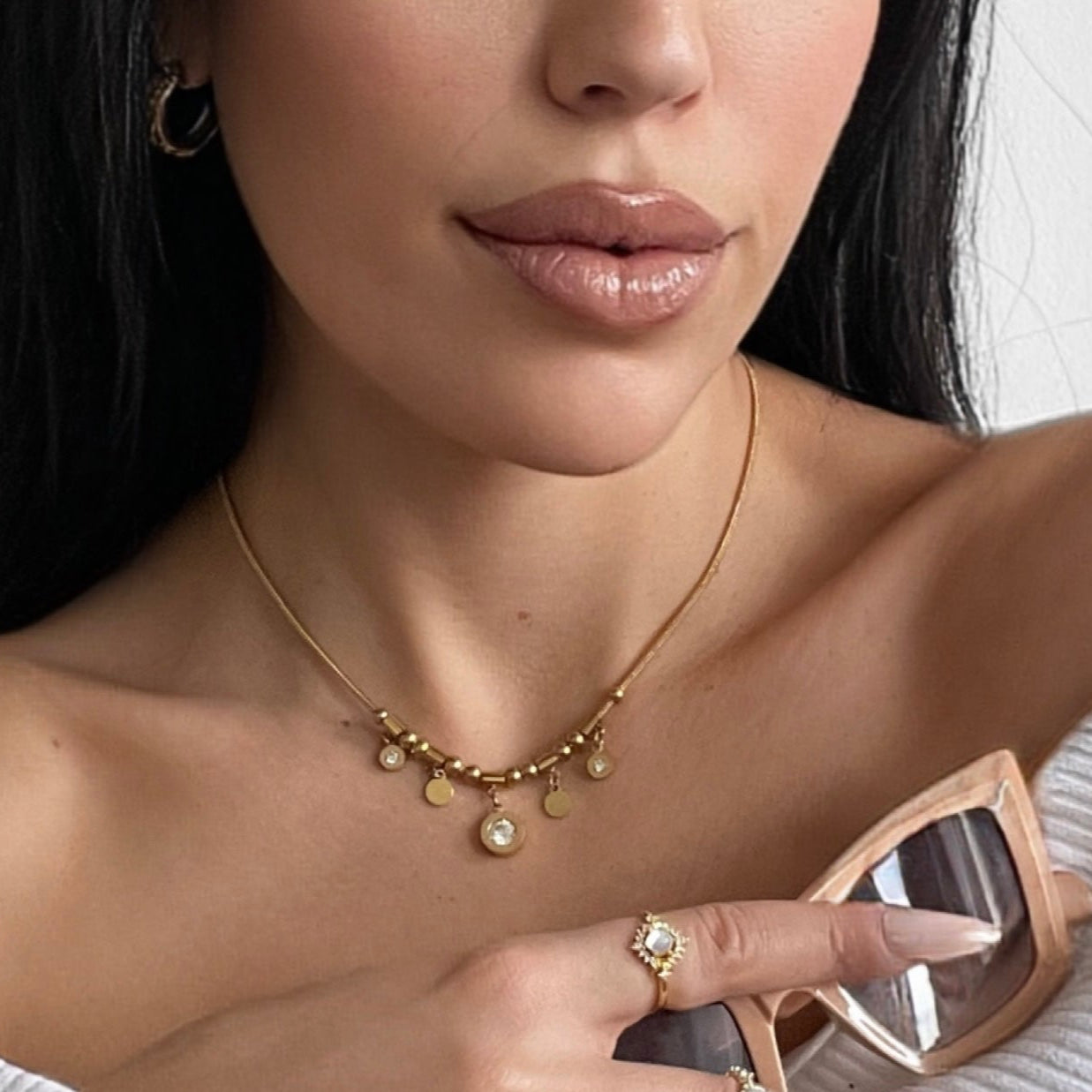 A close-up image of a woman's neck wearing a gold charm necklace with multiple circular charms.