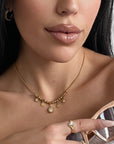A close-up image of a woman's neck wearing a gold charm necklace with multiple circular charms.
