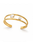 A gold open cuff ring featuring two small bezel-set clear stones, displayed on a clean white background.