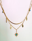 An 18k gold plated necklace with a sunburst pendant and layered chains, featuring small charms including an evil eye and lightning bolt, displayed against a light background.