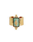 A gold-colored wide band ring featuring a rectangular turquoise crystal with intricate detailing on the sides.