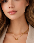 Woman wearing a gold necklace with a subtle design, dressed in a beige blazer and white top.