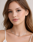 Woman wearing a silver necklace against a plain background