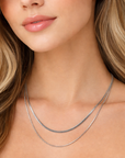 Close-up of a woman wearing a silver necklace with a plain background