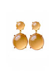 A pair of gold drop earrings featuring large, smooth oval amber-colored gemstones and smaller round studs above them, set against a plain white background.