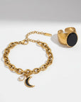 Gold bracelet with moon charm and gold ring with black stone on a white background