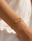 A close-up of a person's wrist wearing a delicate gold double-band bracelet with a star and crescent moon design, styled with a white textured dress.