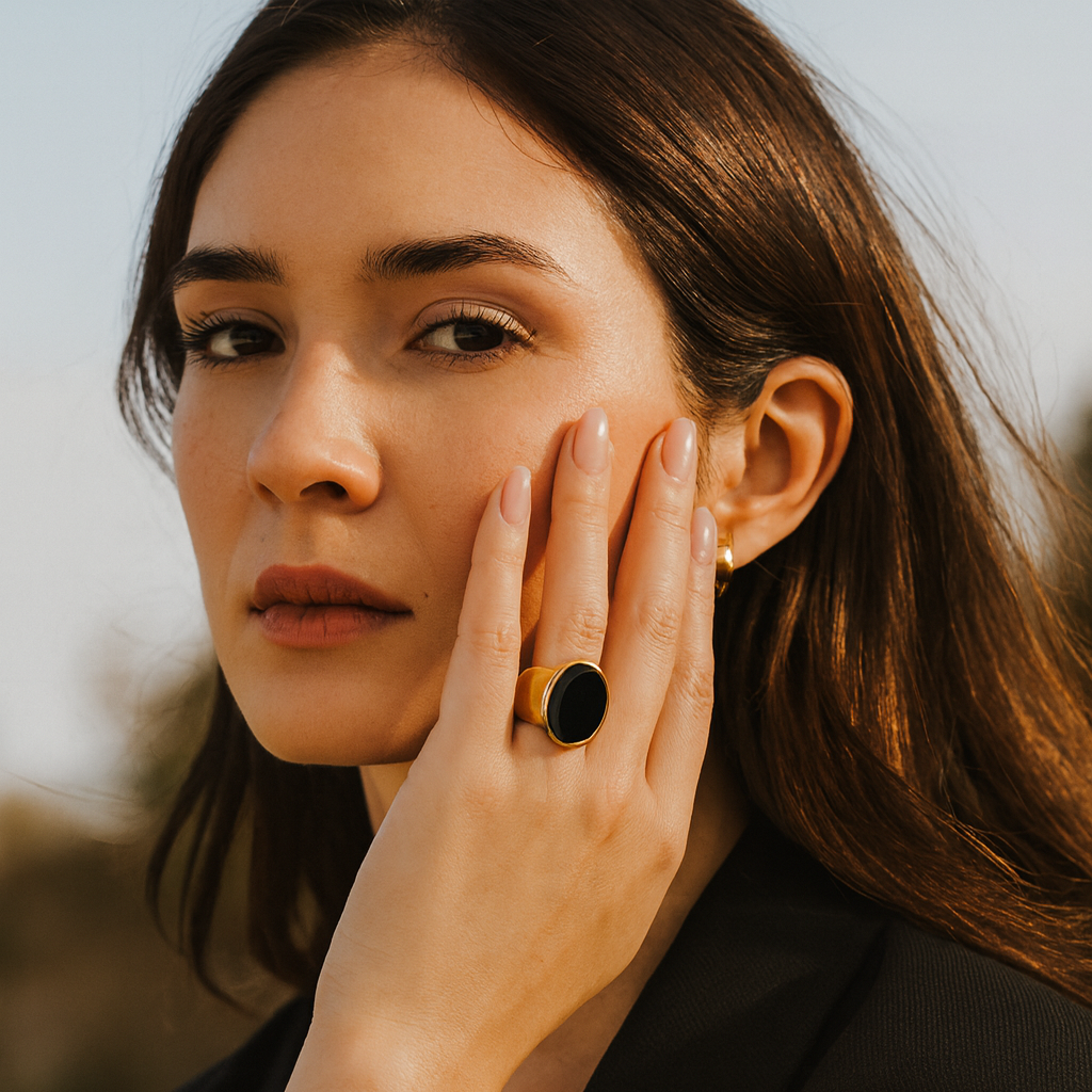 Woman wearing a black ring with a yellow stone, touching her face outdoors.