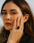 Woman wearing a black ring with a yellow stone, touching her face outdoors.
