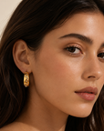 Close-up of a woman wearing gold hoop earrings with a neutral background