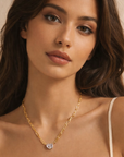 Woman wearing a gold necklace with a clear pendant against a neutral background