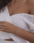 Woman wearing a gold bracelet with a heart charm on a blurred background