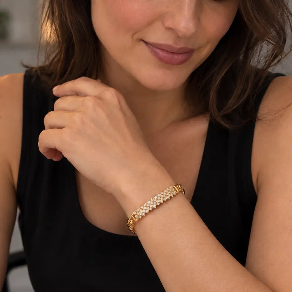 A woman wearing a gold chain-link bracelet with small clear stones, shown in a close-up lifestyle shot while wearing a black sleeveless top.