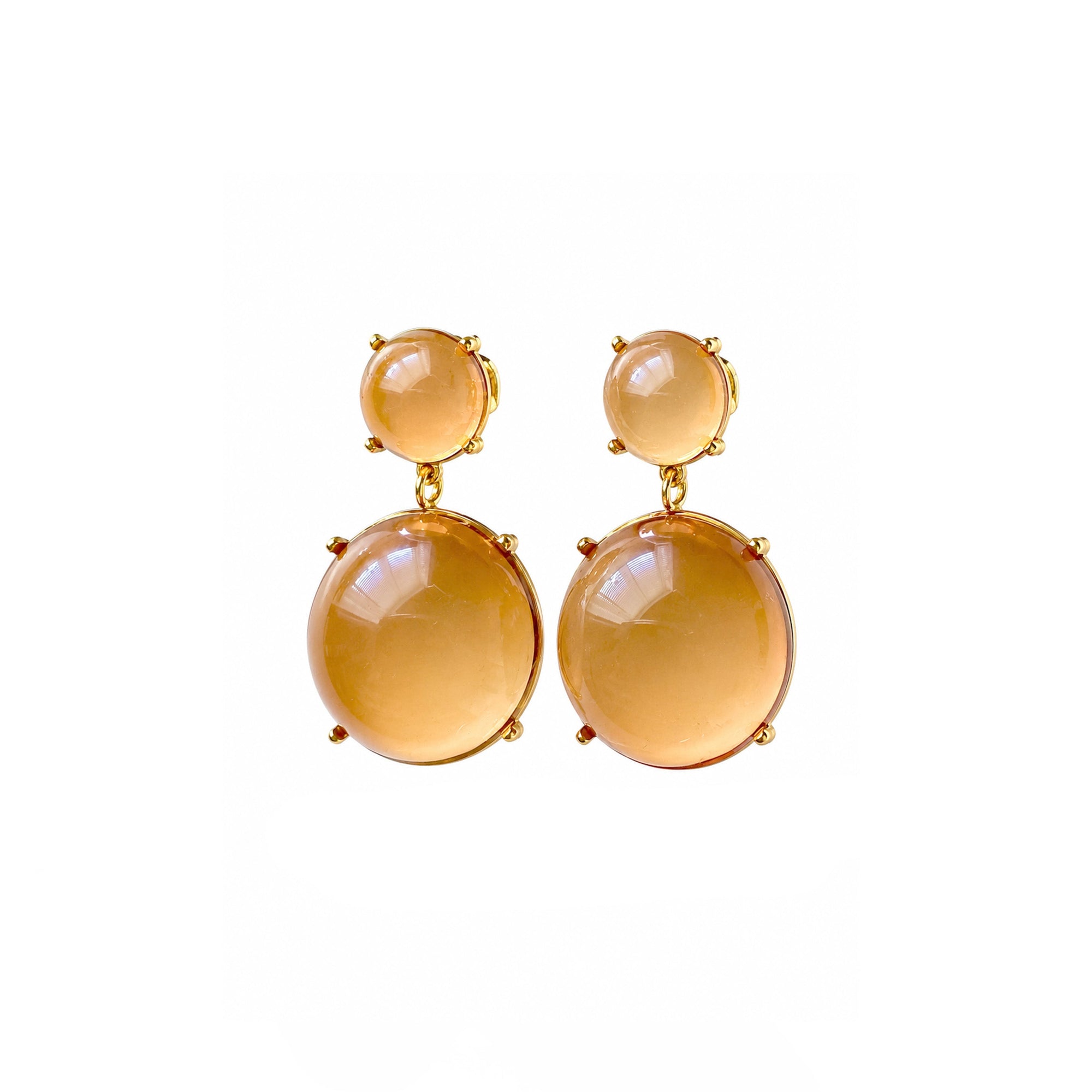 A pair of gold drop earrings featuring large, smooth oval amber-colored gemstones and smaller round studs above them, set against a plain white background.
